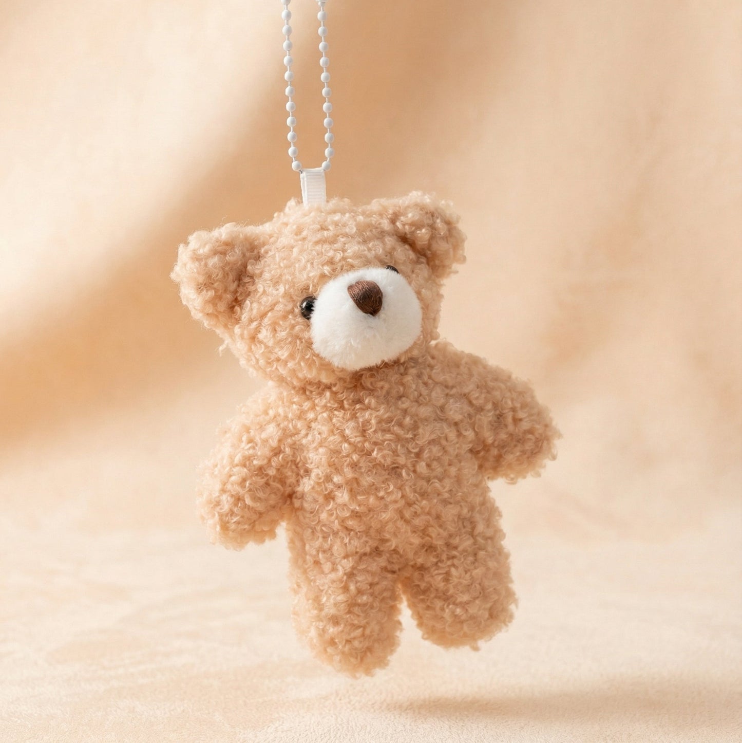 Small teddy bear keychain on a soft beige background