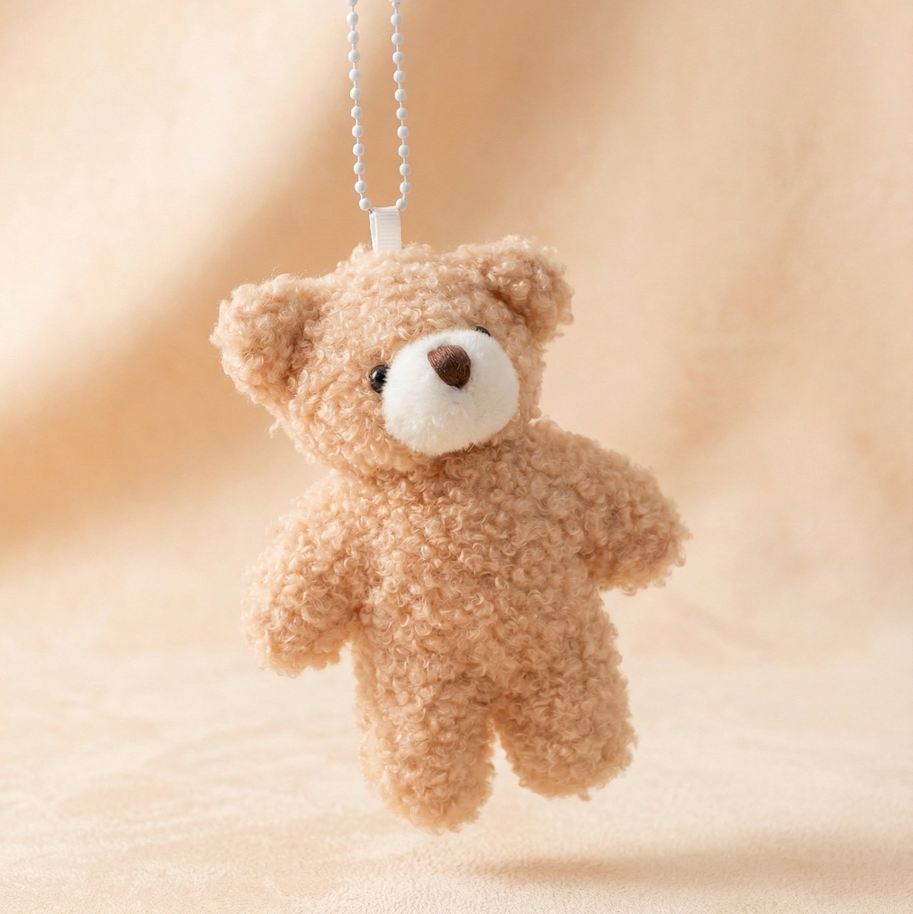 Small teddy bear keychain on a soft beige background