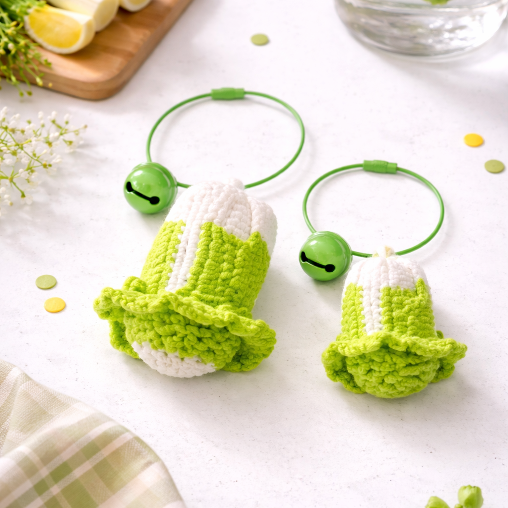 Two green and white crocheted keychains on a white surface with lemons and a glass of water in the background.