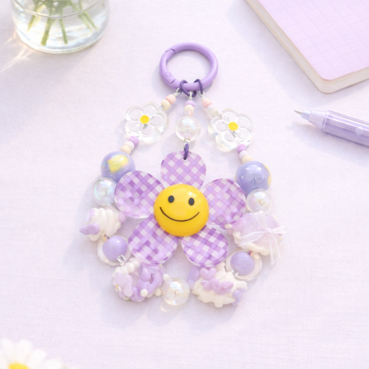 Purple flower-shaped keychain with a smiley face on a light purple background