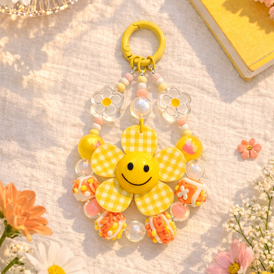 Yellow flower-shaped keychain with smiley face on a light surface with flowers around