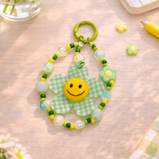 Decorative keychain with a smiley face design on a table with flowers and a notebook.