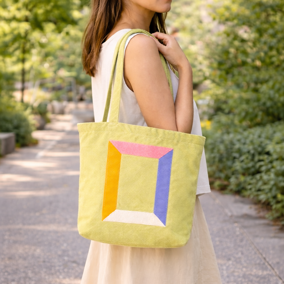 Woman holding a yellow tote bag with colorful geometric design outdoors.