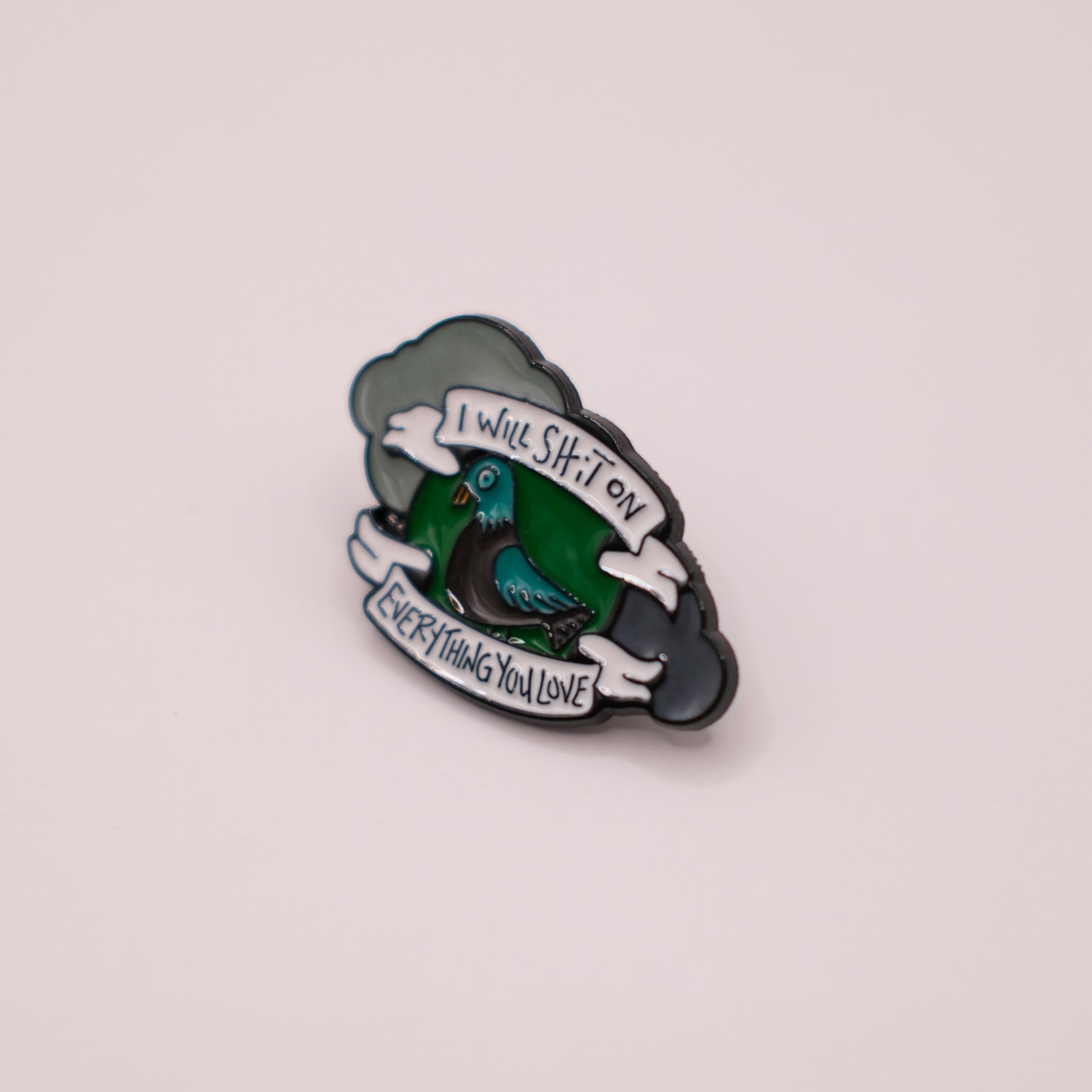 Enamel pin with a green bird design and text on a light gray background