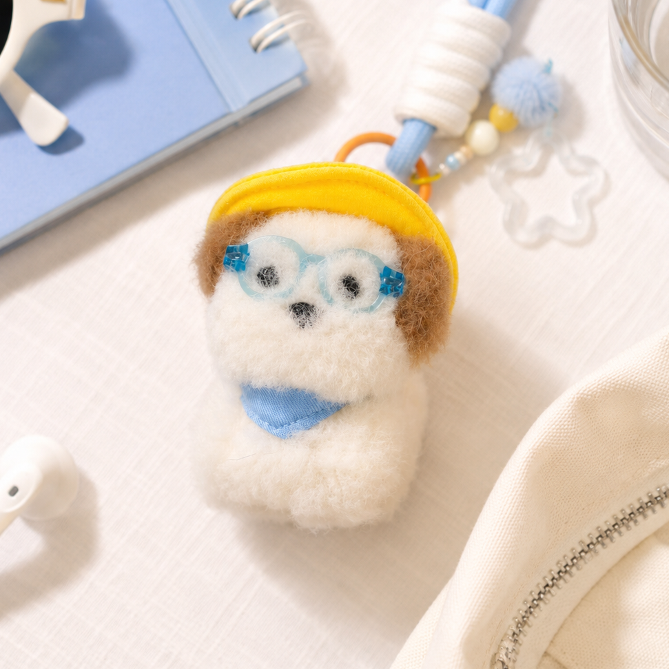 Small plush toy with a yellow hat on a desk with a notebook, sunglasses, and water bottle.