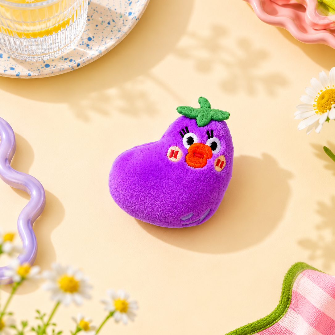 Purple eggplant plush brooch with a face on a yellow background with flowers and a glass of lemonade.