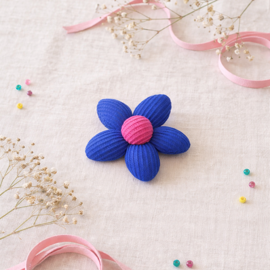 Blue and pink flower-shaped object on a textured surface with ribbons and small flowers.