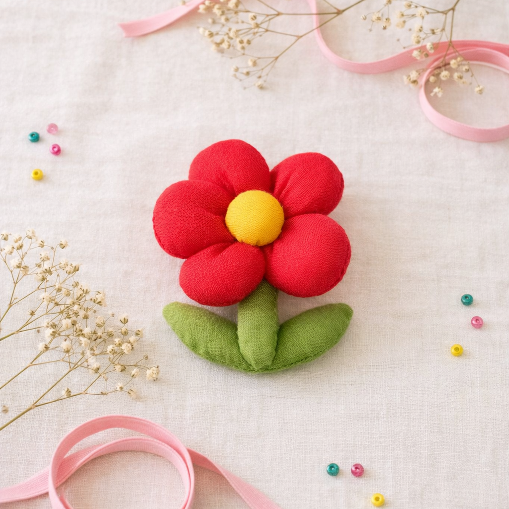Felt flower with a yellow center and red petals on a white background with pink ribbons and small flowers.