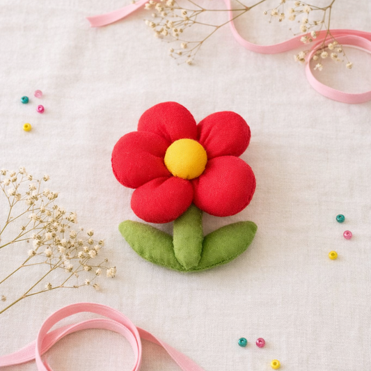 Felt flower with a yellow center and red petals on a white background with pink ribbons and small flowers.