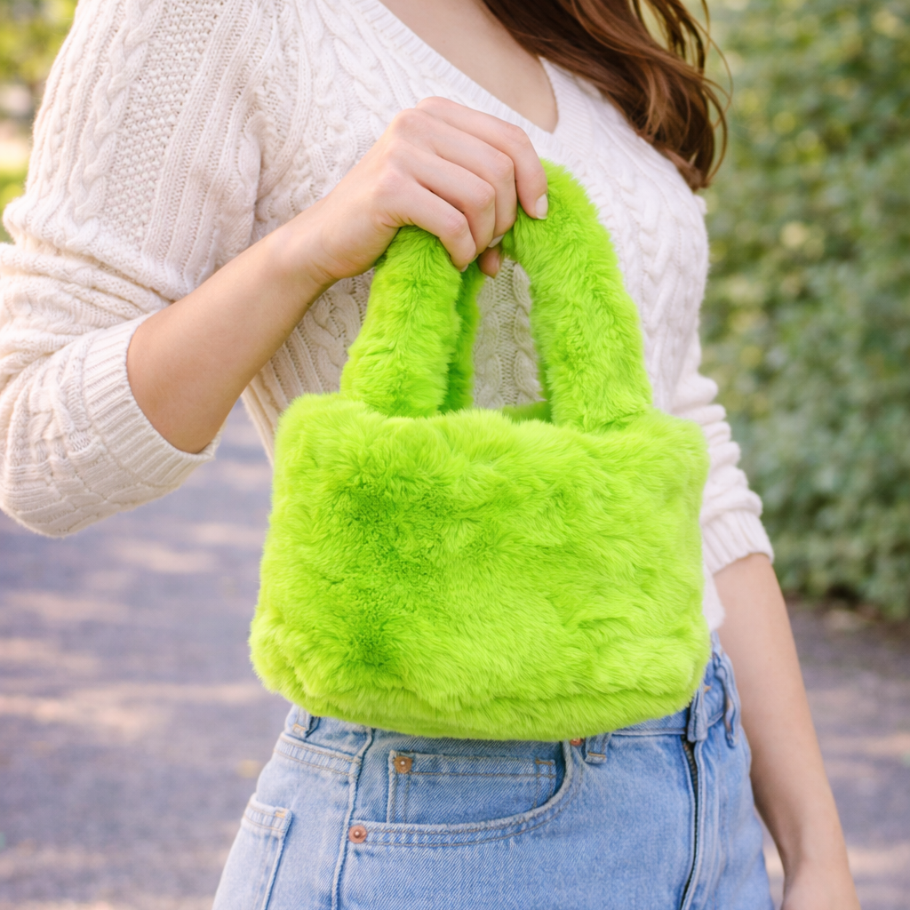 Person holding a bright green fluffy handbag outdoors