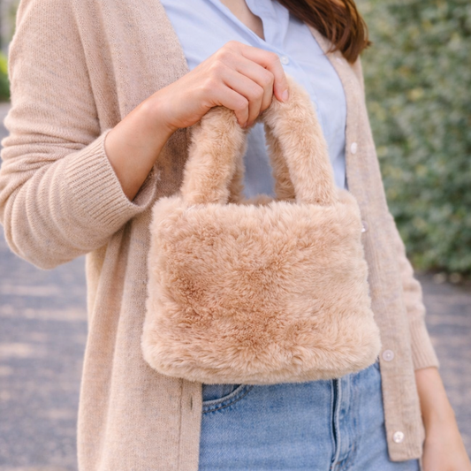 Woman holding a fluffy beige handbag outdoors