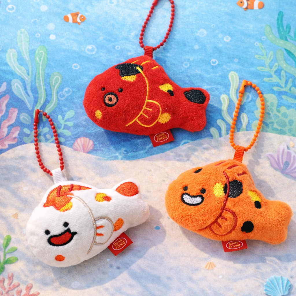 Three colorful fish-shaped keychains on a blue underwater background with fish and coral.