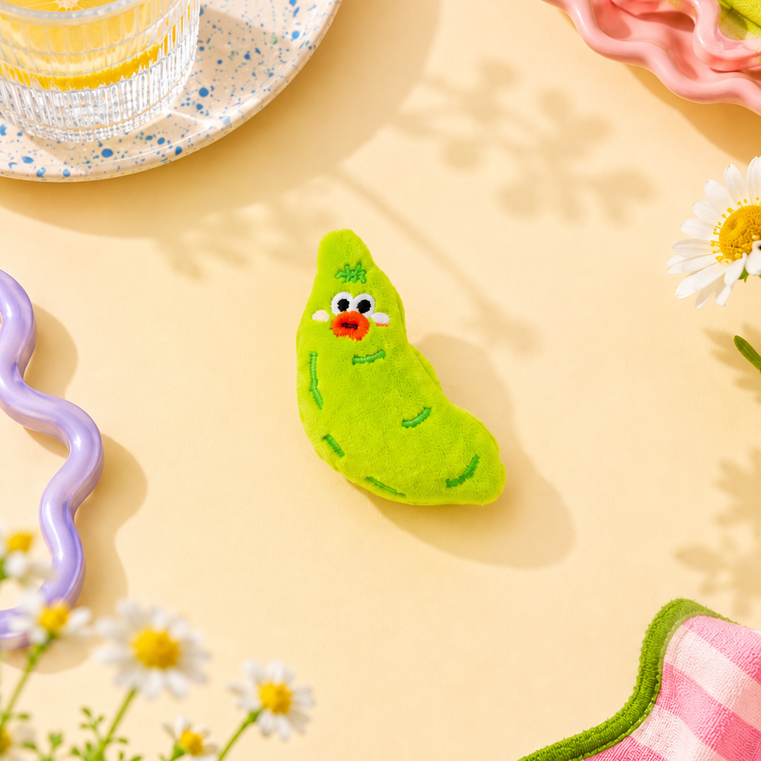 Green plush toy resembling a pea on a yellow surface with flowers and a glass of water.