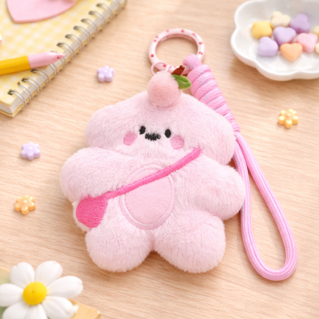 Pink plush keychain with a face on a wooden surface with stationery items.