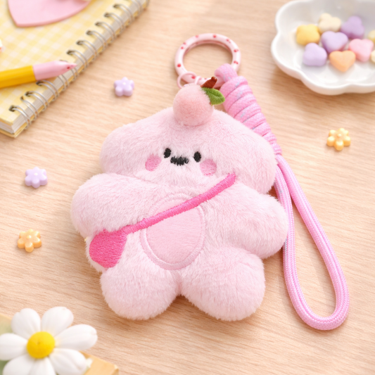 Pink plush keychain with a face on a wooden surface with stationery items.