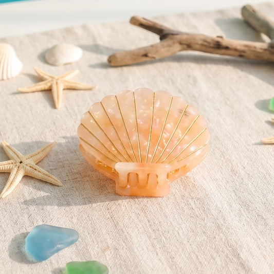 Seashell hair claw, starfish, and sea glass on a sandy surface with a blue water background