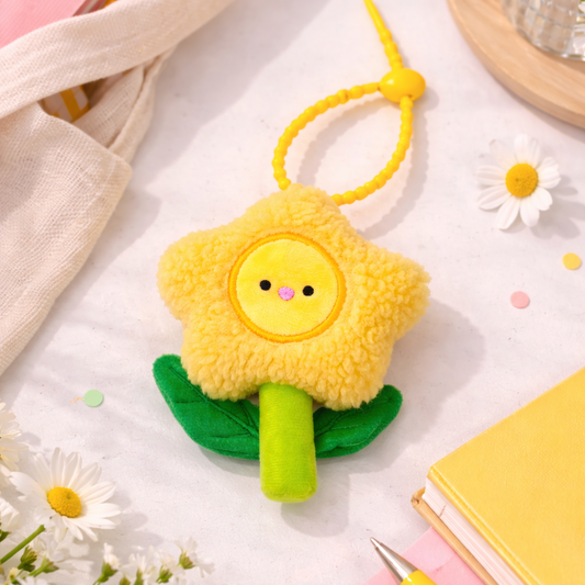 Yellow sun-shaped keychain with a face on a light surface with flowers and stationery items.