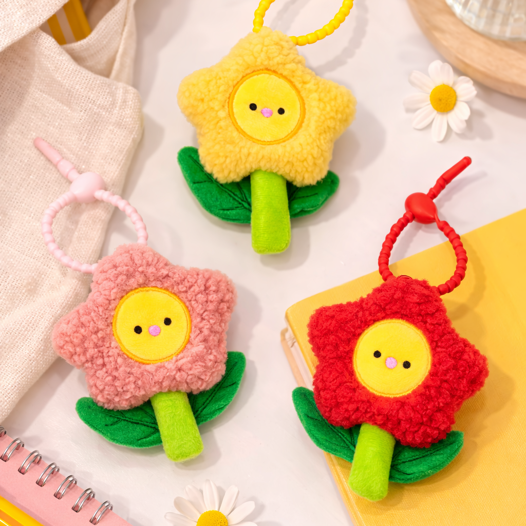 Three colorful flower-shaped keychains on a light surface with flowers and stationery items.